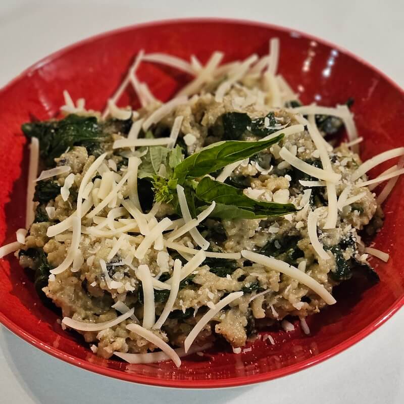 A red bowl filled with a creamy pasta dish, topped with shredded cheese and garnished with fresh basil leaves.